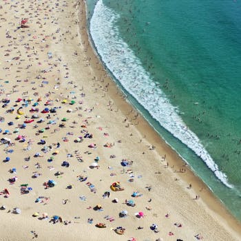 Stunning aerial view of crowded Nazaré beach with colorful umbrellas and clear waves.