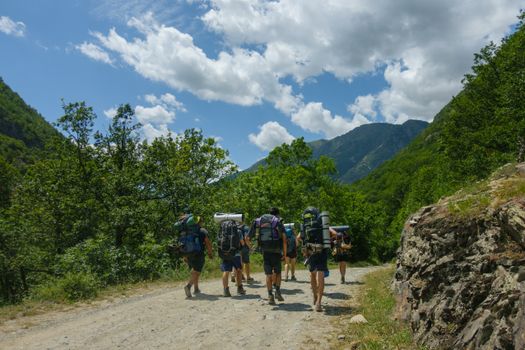 A group of backpackers walking on a trail surrounded by lush mountains on a sunny day.