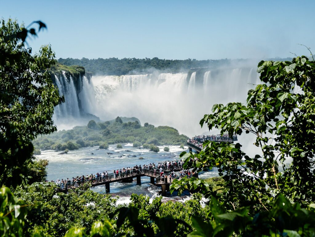 Tourists enjoying the magnificent view of Iguazu Falls from a wooden deck surrounded by lush greenery.