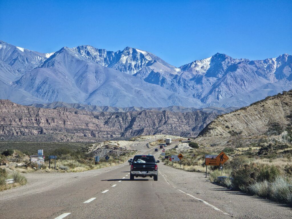A breathtaking drive through a mountain landscape with snow-capped peaks under a clear blue sky.