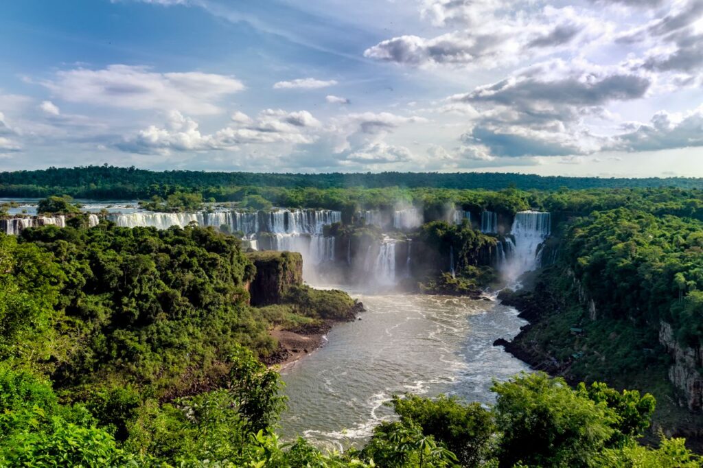 Breathtaking aerial view of cascading Iguazu Falls surrounded by lush rainforest, under a vibrant summer sky.