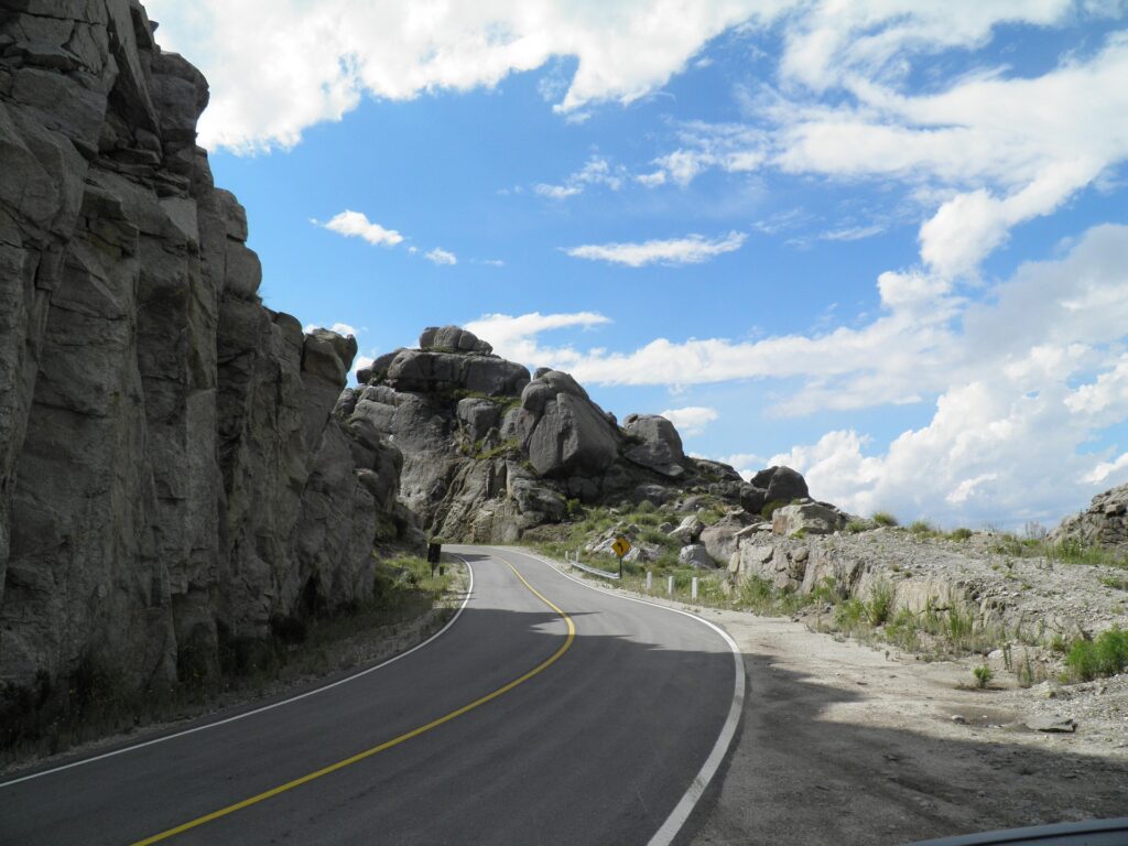 imagen de un paquete de travelcas a Villa de Merlo en San Luis, de una ruta co montañas rocosas en su costado izquierdo, es una ruta que justo entra en una curva